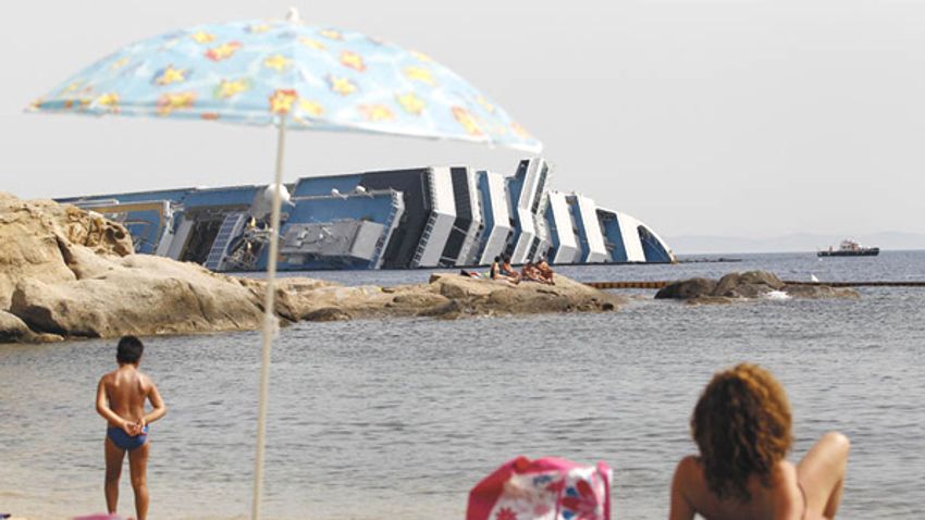Vacationers stand in front of the wreckage of capsized cruise liner Costa Concordia near the harbour of Giglio Porto
