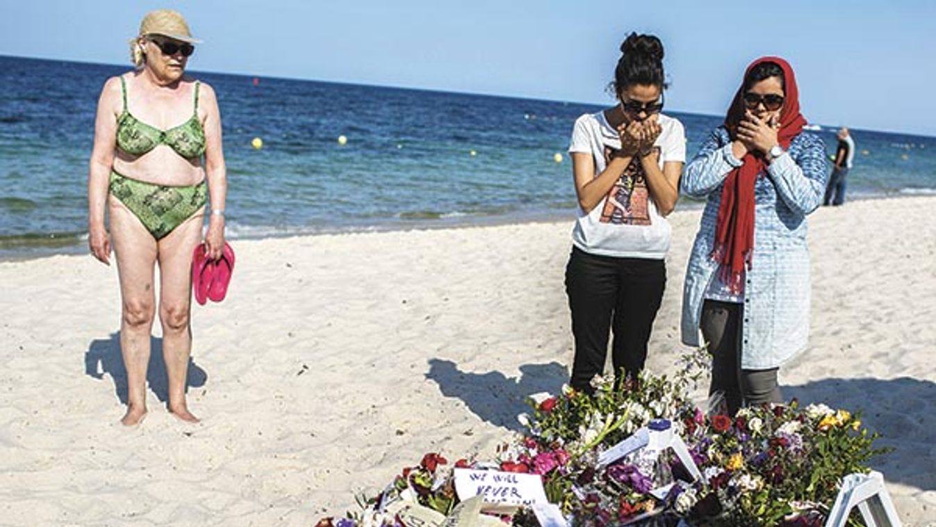 Women pray near bouquets of flowers laid on the beach of the Imperial Marhaba resort, which was attacked by a gunman, in Sousse, Tunisia