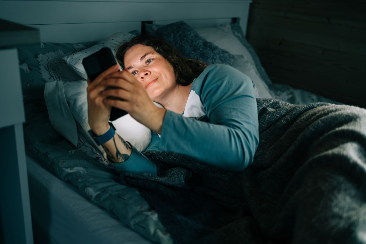 Smiling woman using smartphone in bed at night