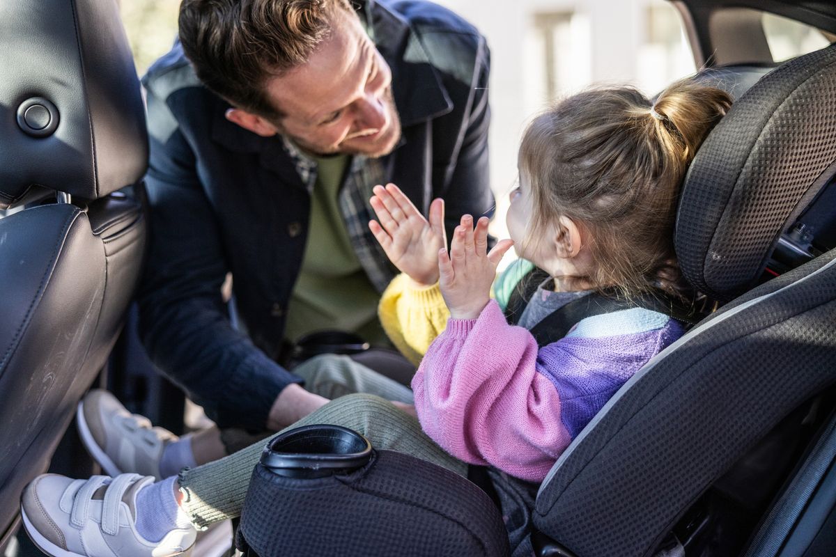 Father buckling toddler daughter in to her car seat
